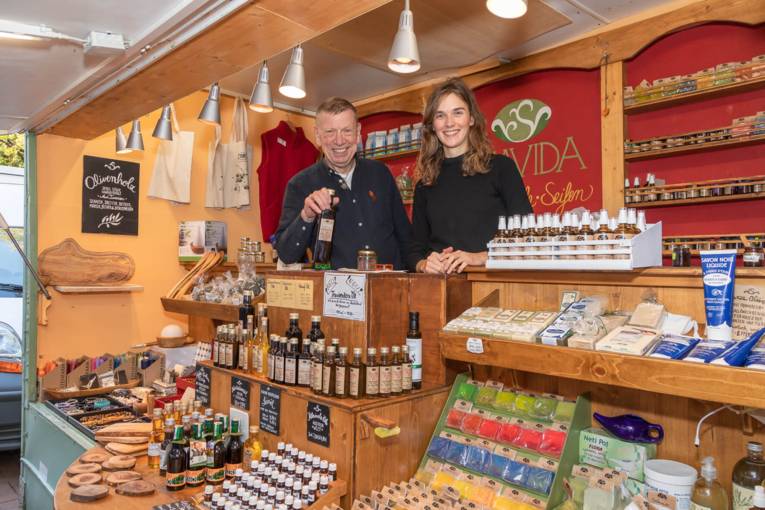 Verkaufspersonal bietet &Ouml;le, Seifen und Tees in einem Marktwagen an.